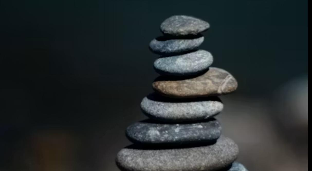 Smooth stones stacked into a balanced tower at sunrise, representing stacking small daily wins