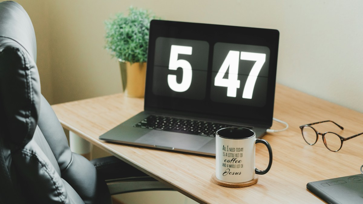 Time management for insurance agents: a laptop clock showing 5:47 on an office desk at the end of the workday